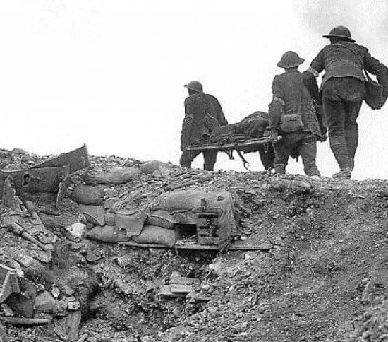 3 men in military uniform carrying a 4th man away on a stretched from the trenches