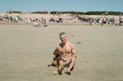 Vintage photograph of a brown dog and a man sitting on the beach