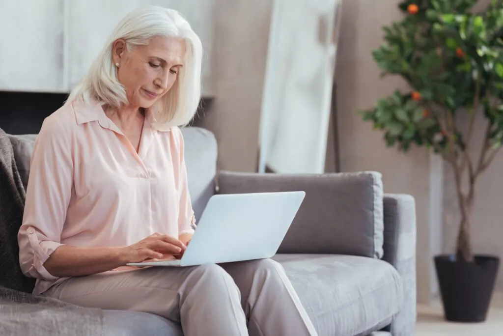 Older woman sitting on a couch typing on a laptop