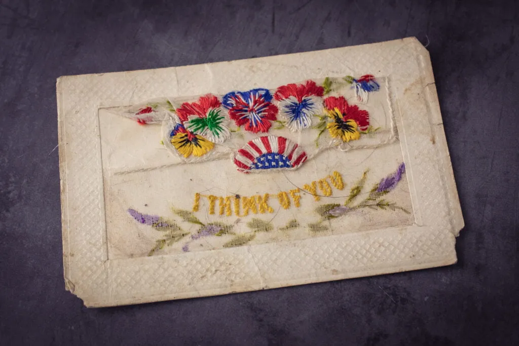 Vintage war postcard with embroidery on lace of flowers and an American flag with the script I think of you