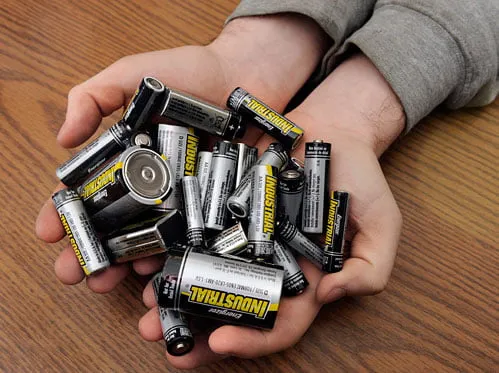 Male hands holding a pile of miscellaneous batteries