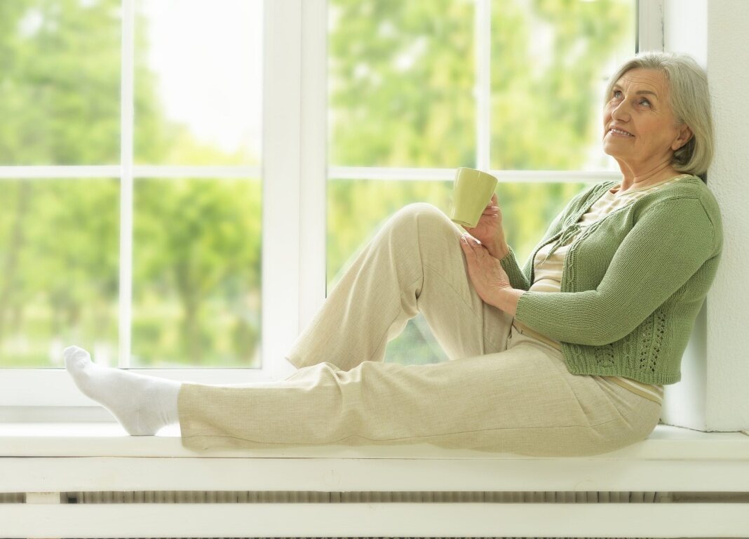 older woman looking happy, sitting on windowsill