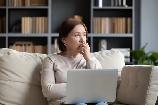 woman on sofa looking worried with a laptop on her lap