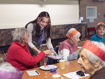 younger woman serving food to older ladies wearing christmas hats