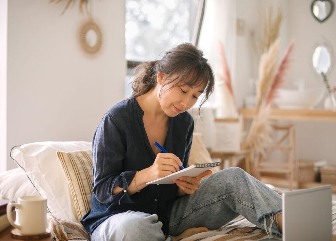 woman sitting on sofa writing on a notepad